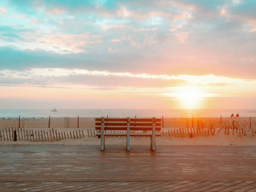 A wooden bench on the Belmar boardwalk facing the ocean at sunrise