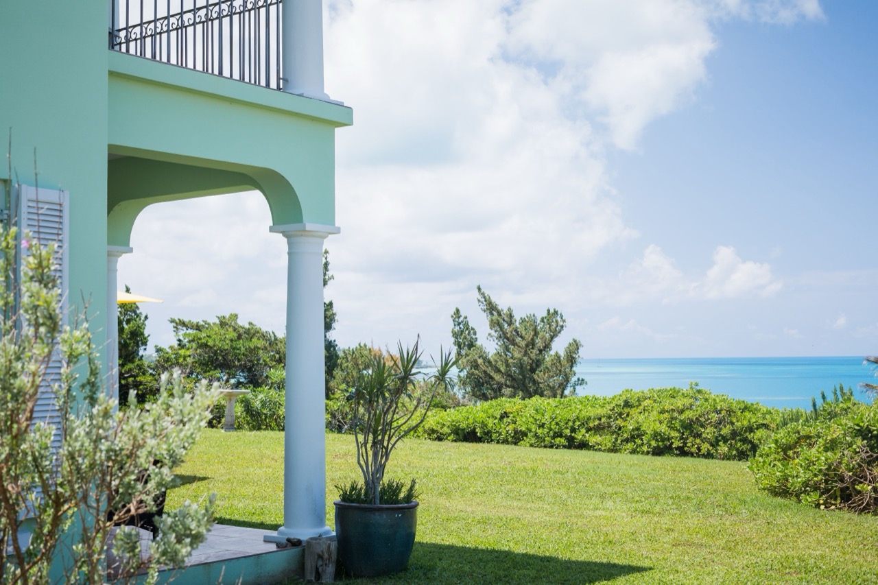 A coastal home with a covered porch looking out over the ocean on a bright summer day
